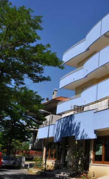 Edificio moderno blu, luminoso e accogliente, circondato da piante verdi e cielo sereno.